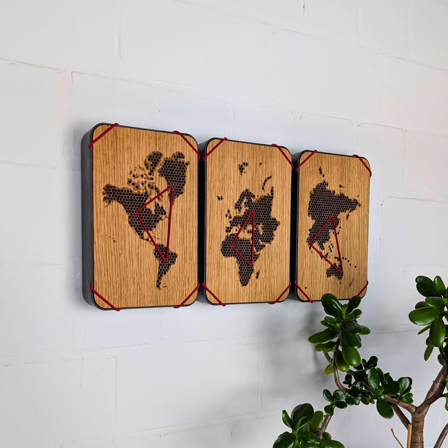 Drei Questlog-Erinnerungsboxen nebeneinander an einer weißen Wand, die Deckel ergeben zusammen eine Weltkarte